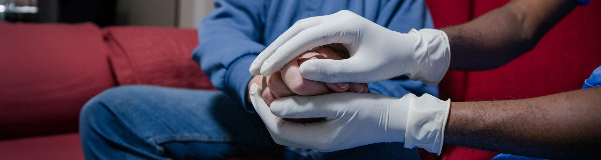 Two people holding hands, one wearing white gloves, sitting on a red couch.